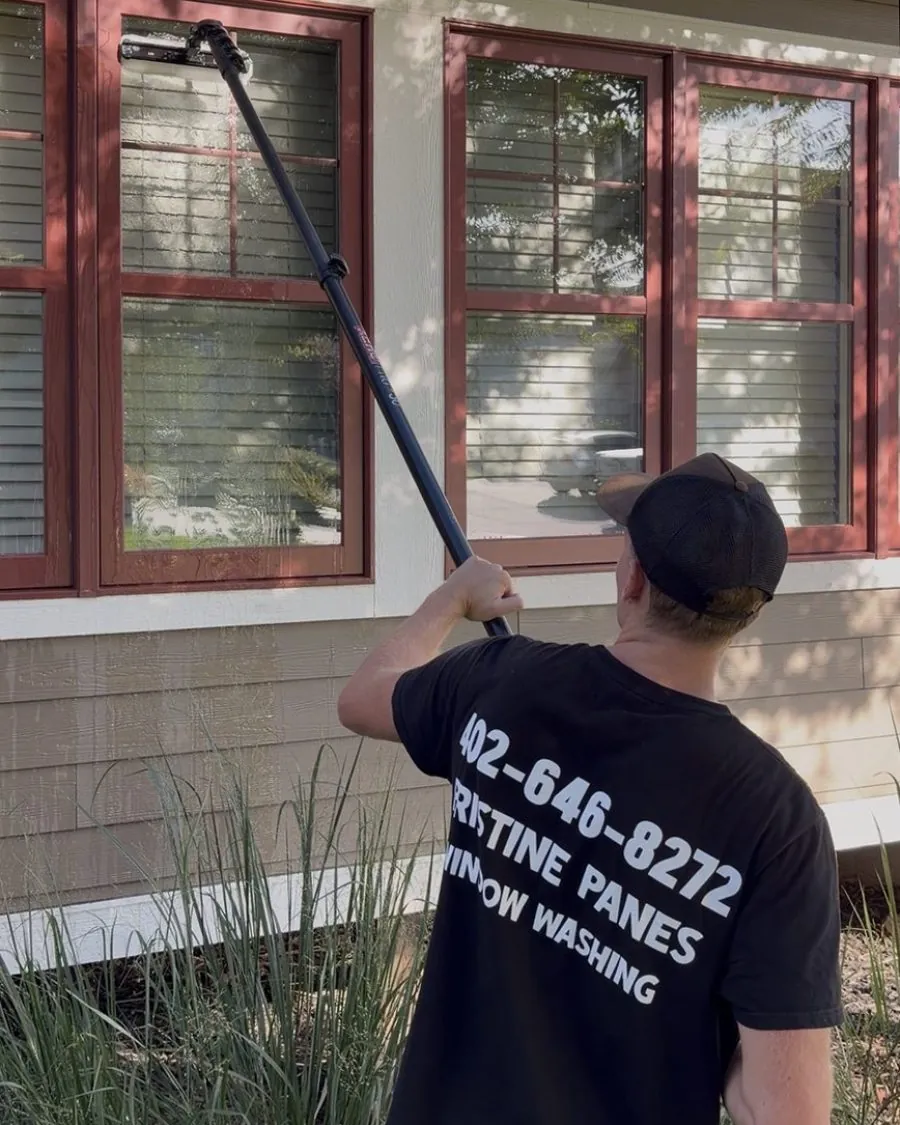 A Pristine Panes technician cleaning a home's windows with a water-fed pole